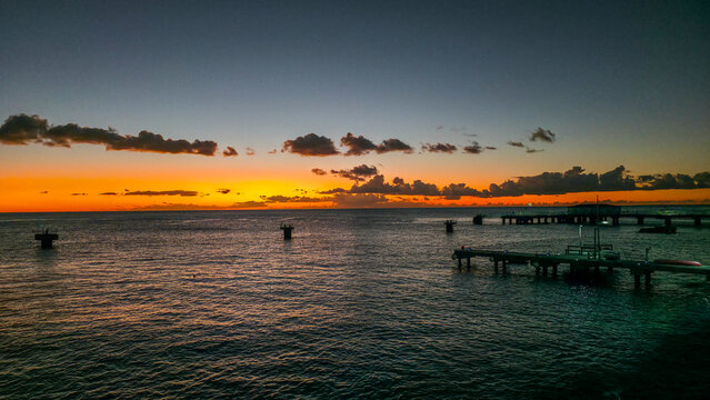 Colors fill the sky as day ends and night begins over the water near a pier at sunset in Roseau, Dominica