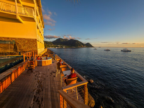 Evening light reflects on water as people relax and boats drift at sunset in a coastal setting near mountains