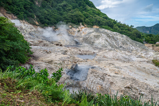 Drive in volcano features steam vents and mineral deposits in landscape with trees and hills in background, found in Saint Lucia