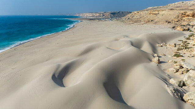 Sand dunes rise by the Indian ocean near Eyl with waves and beach extending under a blue sky in Puntland, Somalia