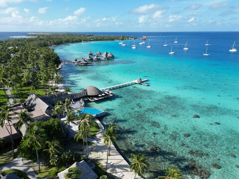 Resort located in clear turquoise water with palm trees and boats in Rangiroa