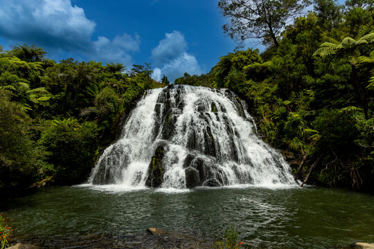 Water cascades down Owharoa Falls, surrounded by trees and vegetation, creating a natural display in Karangahake Gorge, North Island New Zealand