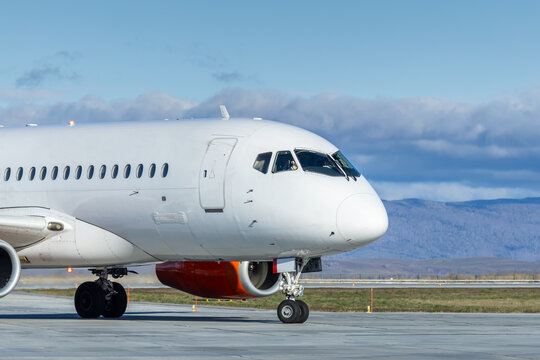 Close up to the front of the white passenger plane taxiing at the airport against a mountain range