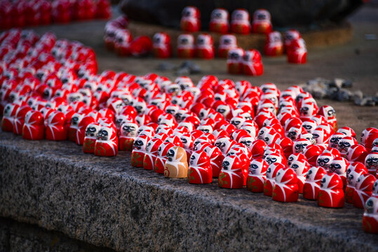 Clusters of Daruma dolls resting on a temple ledge in Minoh, Japan during a quiet moment of reflection and spiritual connection
