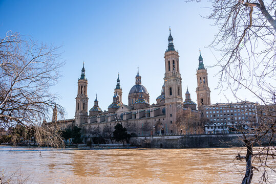 Basilica del Pilar rises above the Ebro River in Zaragoza with bare trees framing the view on a clear day