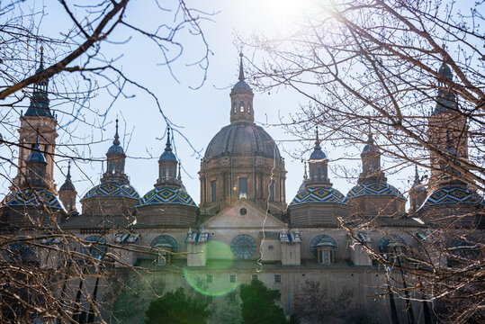 Intricate domes of Baslica del Pilar with sunlight through winter trees in Zaragoza, Spain