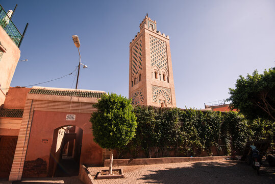 Distinctive minaret of mosque rises above pink walls and shaded archway in vibrant Marrakech