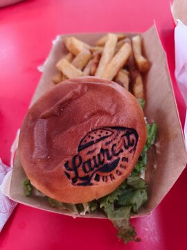 Royan, France - May 31, 2026: Charente-Maritime. Nouvelle-Aquitaine. Burger with branded bun and lettuce served with French fries in a cardboard tray on a red table
