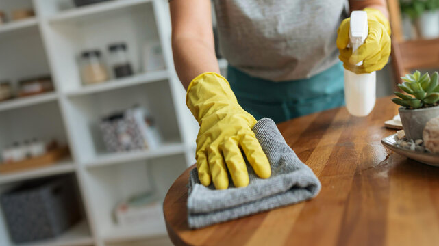 Person cleaning wooden table with spray bottle and cloth for home maintenance and hygiene