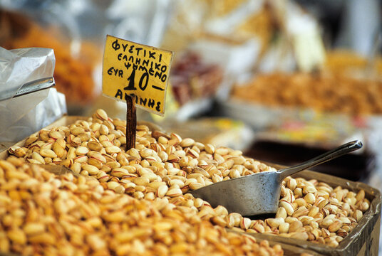Roasted pistachios displayed at a market stall with a price sign in Greece