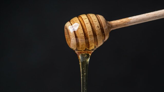 Golden honey dripping from a wooden dipper on a dark black background