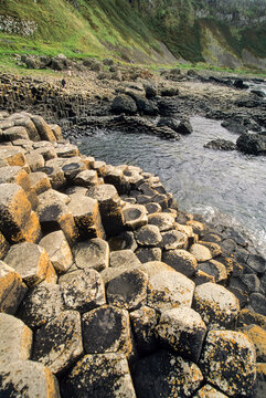 Unique rock formations line the shoreline near water at Giants Causeway during daylight in County Antrim, Northern Ireland