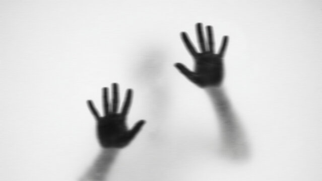 Human hands silhouette behind frosted glass, mysterious shadow of palms on white background.