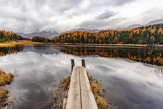 Autumn reflections seen from a pier at Lej da Staz, St. Moritz, Engadin, Graubunden, Switzerland