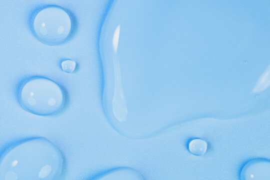 Macro shot of clear elongated water drops with light reflections on blue textured surface. Abstract wet background perfect for skin hydration, cosmetics, medical industries, purity, product backdrop.