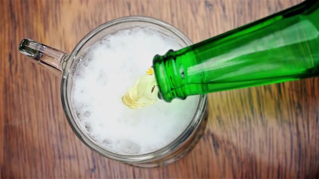 Top Down View of Cold Beer Pouring from Green Bottle into Glass Mug