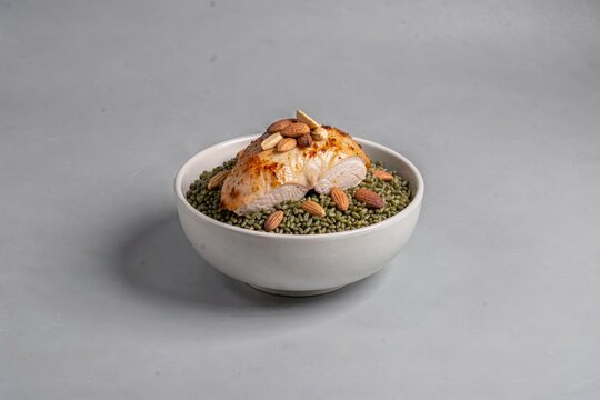 Bowl of freekeh with chicken topped with almonds and bread, placed on plain grey background. Concept of smoked green wheat with chicken nuts.