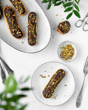 Chocolate glazed eclairs with chopped pistachios on white plates