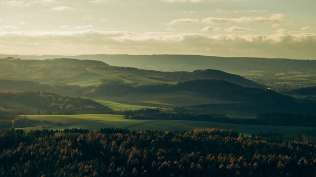 Aerial view of rolling hills, forests, and agricultural fields bathed in soft golden hour light in Czech Republic.