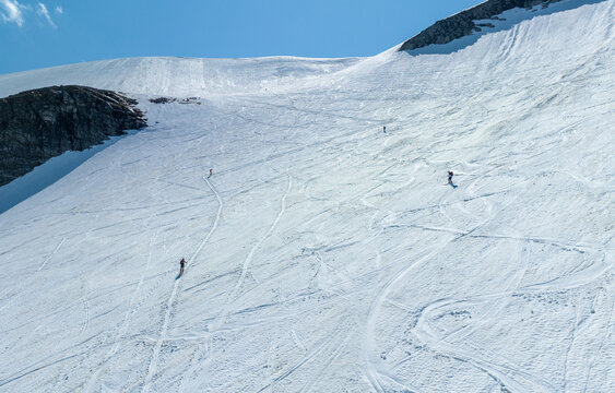 Aerial view of Alnestinden mountain with skiers traversing the snowy slopes under a clear blue sky in Andalsnes, More og Romsdal, Norway.