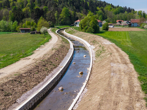 Aerial view shows river channel widening and raised embankments in a rural area.
