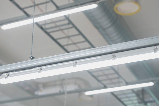 Suspended modular LED lighting fixture with continuous trunking rail installed on a ceiling framework in a modern industrial warehouse