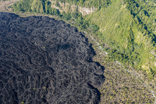 Aerial view of a vast black lava field contrasting with the lush green forest and rugged terrain in Kuta Selatan, Bali, Indonesia.