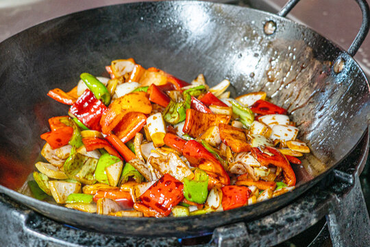 Professional chef hands tossing sliced beef and bell peppers in a hot wok for a black pepper beef dish.