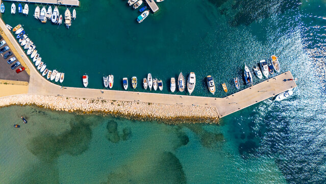 Aerial view of the marina in Rab with numerous boats moored along the stone pier, surrounded by clear turquoise waters in Rab, Primorje-Gorski Kotar, Croatia.