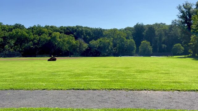 Lawn mower cutting grass on green field in public park