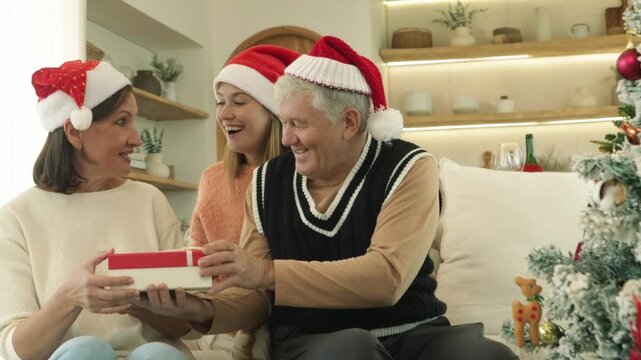 Christmas Day : Warm family parents and their adult daughter are celebrating Christmas at home mother surprises her daughter gift box all three are happy faces beaming smiles enjoying the gifts.