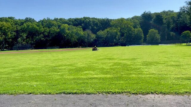 Riding lawn mower cutting grass on sports field in park