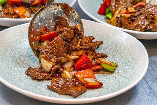 Professional chef hands tossing sliced beef and bell peppers in a hot wok for a black pepper beef dish.