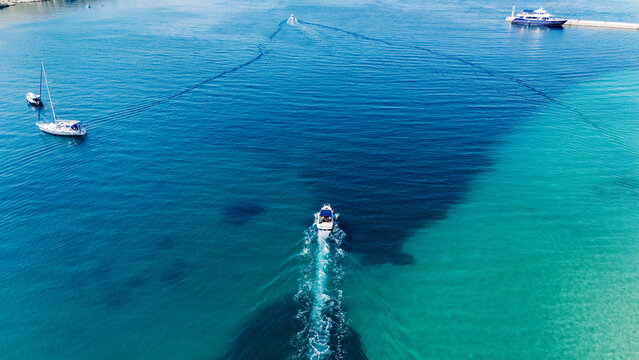 Aerial view of a motorboat leaving a wake in the clear turquoise and deep blue waters near the coast of Rab, Primorje-Gorski Kotar, Croatia.