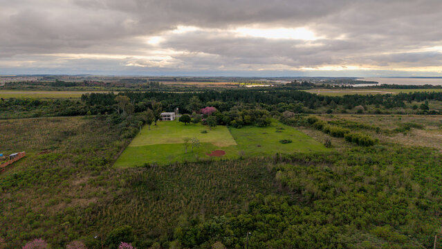 Aerial view of a new residential development surrounded by lush green fields, scattered trees, and native vegetation under a cloudy sky in Posadas, Misiones Province, Argentina.