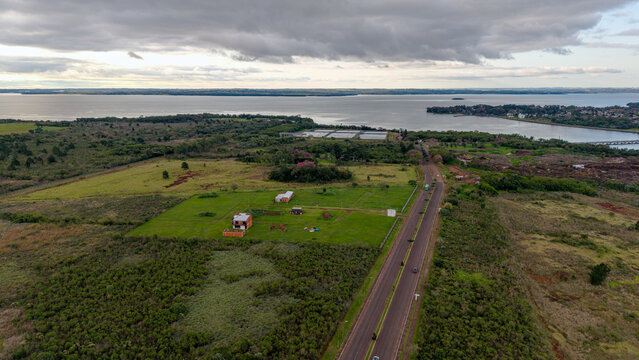 Aerial view of a new residential development with scattered houses, green fields, and a paved road near the Parana River in Posadas, Misiones Province, Argentina.
