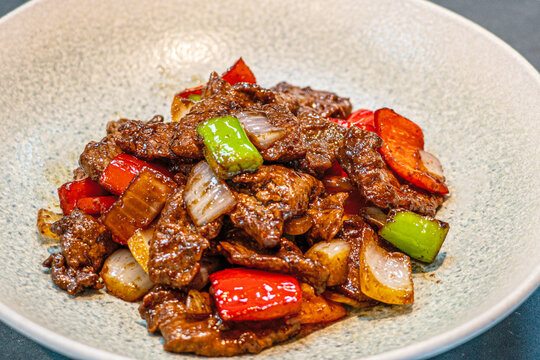 Professional chef hands tossing sliced beef and bell peppers in a hot wok for a black pepper beef dish.