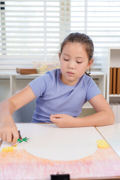 Caucasian elementary girl student using crayons to color large artwork at classroom desk representing creativity imagination dedication concentration childhood artistic educational development