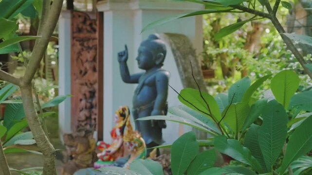 Buddha statue by tropical foliage in peaceful temple garden, Sacred Buddhist shrine framed by green leaves in tranquil Asian spiritual sanctuary 4k