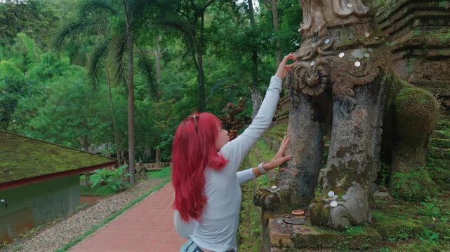 Woman placing coins on ancient temple statue in Chiang Mai, Female making offering at moss covered Buddhist shrine during cultural Wat Phra Lat temple visit in Thailand 4k