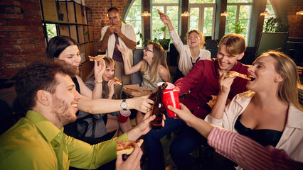 Obraz premium Coworkers toasting with drinks while sharing pizza at office party. Concept of beverage delivery pages, corporate catering services and staff event websites.