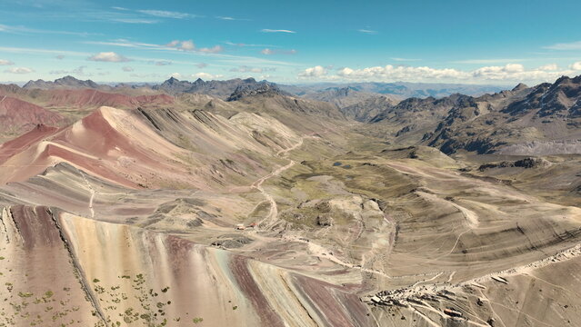 Aerial view of the colorful striped slopes of Vinicunca, or Rainbow Mountain, with rugged Andean terrain and winding trails, Quispicanchi Province, Cusco, Peru.