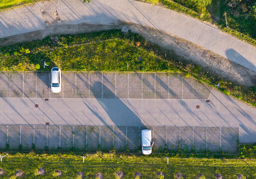 Aerial view of a parking lot in Dabrowa with two parked cars, paved parking spaces, and surrounding green grass in Gdynia, Pomeranian Voivodeshi, Poland.