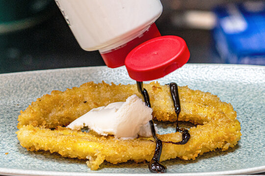  Professional chef hands plating a gourmet grilled banana dessert with vanilla ice cream and rich chocolate sauce.
