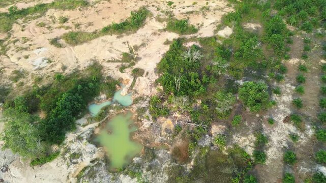 Aerial top-down view of abandoned mining pits filled with acidic water near young oil palm plantation, showing environmental damage and land degradation