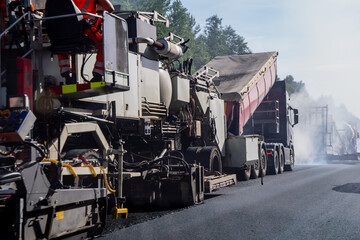 Naklejka premium Heavy asphalt paving machine spreading hot mix asphalt material on a roadway during highway repaving and civil infrastructure development