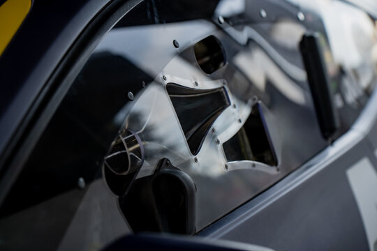 Racing car polycarbonate side window featuring integrated NACA duct and ventilation slider for cockpit airflow management in paddock
