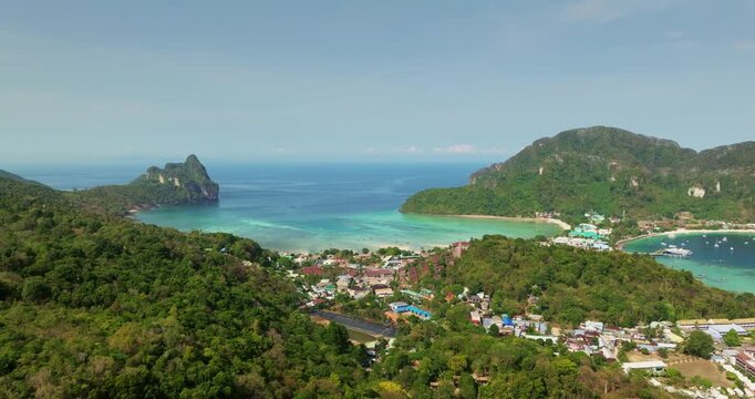 Ko Phi Phi Don island bustling town, lush green hills and tranquil bays with clear turquoise water, dramatic limestone cliffs under a bright sky. Thailand travel tourist destination. Aerial view shot