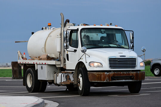 Portable toilet rental service truck with vacuum tank driving on a roadway, illustrating sanitation services, waste removal, equipment maintenance, and commercial fleet operations