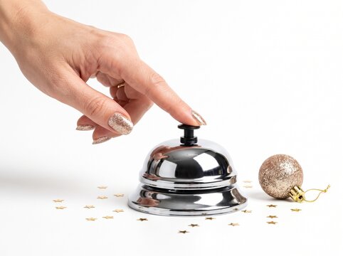 Woman hand with glitter polish ringing chrome desk bell with gold star confetti isolated on white